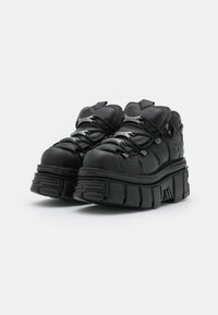 Black platform shoes with rounded toes, padded collar, and textured rubber soles. Features metal accents and contrasting laces.