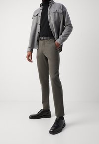 Šedá flanelová košile přes černý rolák, v kombinaci s olivově zelenými slim-fit kalhotami a černými koženými botami. Obsahuje černý pásek.