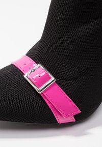 Musta sukkakorkokenkä, jossa on ribat tekstuuri. Siinä on kiiltävä vaaleanpunainen hihna ja hopeinen solkiyksityiskohta. Teräväkärkinen muotoilu korostaa eleganssia.