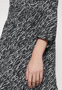 Schwarz-weiß gemustertes Kleid mit fließendem Design, das einen lockeren Schnitt, halblange Ärmel und weichen Stofftexturen aufweist.