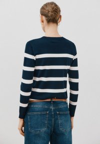 Pullover a righe navy con strisce orizzontali bianche, scollatura rotonda e maniche lunghe, abbinato a jeans in denim blu con tasche posteriori.