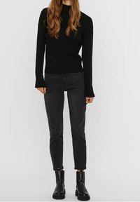 Pull en maille noire à côtes avec des manches longues, associé à un jean noir fuselé et des bottes noires à hauteur de cheville. Tenue simple et monochrome.