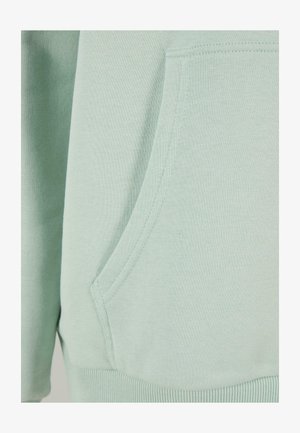 Šviesiai žalia džemperio medžiaga su priekine kišenėle. Audinys yra minkštas, o siūlės tvarkingai užbaigtos. Apvalus kraštas apačioje.