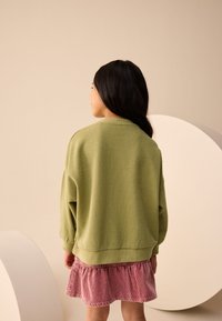 Grøn tekstureret sweatshirt med lange ærmer, kombineret med et lyserødt fløjlsrullet skørt. Enkel design, blødt stof og afslappet pasform.