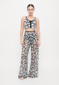Crop top a maniche corte con motivo floreale in bianco e nero, dotato di lacci regolabili sul davanti, abbinato a pantaloni palazzo trasparenti con design a gamba larga.