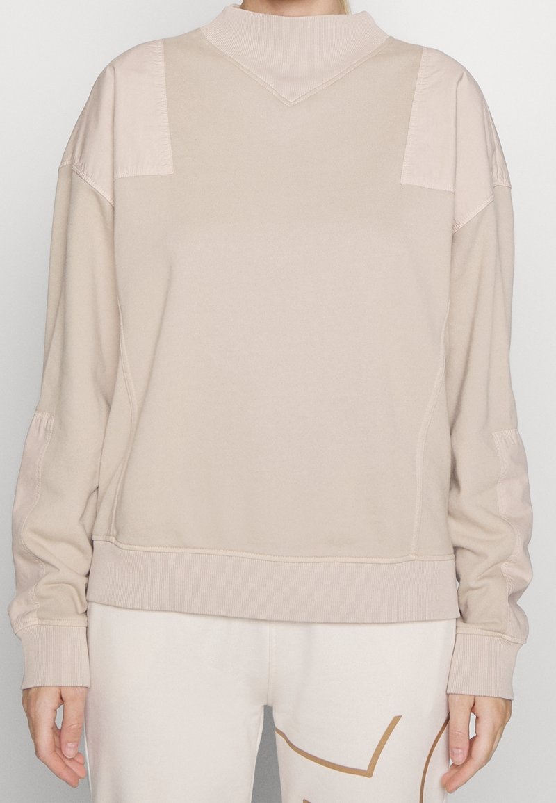 Beige crewneck sweatshirt with textured shoulder panels, ribbed cuffs, and hem; smooth material with a relaxed fit, minimalistic design.