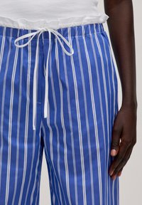 Blauwe en witte gestreepte broek met een trekkoord in de taille, met een gladde stoftextuur. Close-up van de tailleband en hand.