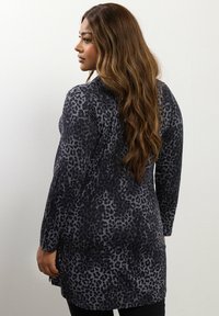 Tunic a maniche lunghe grigia con stampa leopardata nera, caratterizzata da una linea dritta e una texture morbida, indossata sopra leggings neri.