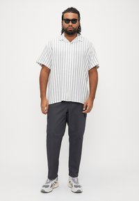 Κοντομάνικο, λευκό ριγέ πουκάμισο με κουμπιά, σε συνδυασμό με σκουρόχρωμο γκρι παντελόνι cargo και γκρι αθλητικά παπούτσια με λεπτομέρειες, ολοκληρώνοντας την casual εμφάνιση.