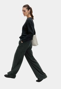 Czarny oversize sweter i ciemnozielone szerokie spodnie z miękkiego materiału; modelka nosi szary plecak o gładkiej fakturze i złożonym designie.