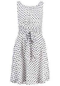 Robe blanche sans manches à pois noirs, col rond, taille cintrée nouée d'un nœud et jupe évasée.