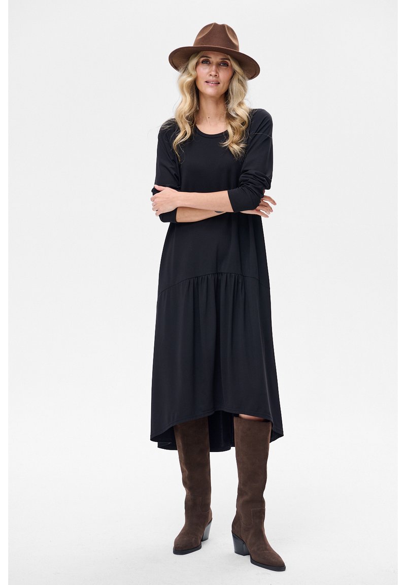 Czarna sukienka z długim rękawem i falbanami u dołu, wykonana z gładkiej tkaniny. Noszona z brązowymi zamszowymi kozakami za kolano i szerokim kapeluszem w kolorze brązowym.