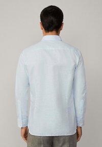 Camicia a maniche lunghe azzurro chiaro con un sottile motivo a righe, colletto button-down e polsini abbottonati. Vestibilità standard, texture morbida.