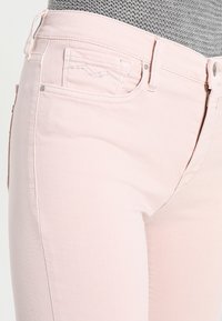 Jeans de mezclilla rosa claro con un diseño clásico de cinco bolsillos y detalles de costura sutiles en el bolsillo delantero. Textura suave, corte ajustado.