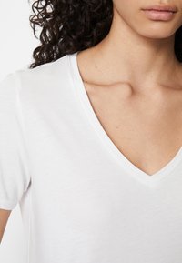 Hvit V-hals t-skjorte med korte ermer, laget av myk, lett stoff. Har en avslappet passform og jevn tekstur.