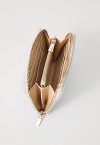 Beige Geldbörse mit goldenem Reißverschluss. Das Innenleben verfügt über mehrere Kartenfächer und ein Reißverschlussfach, aus strukturiertem Material mit glatter Oberfläche.