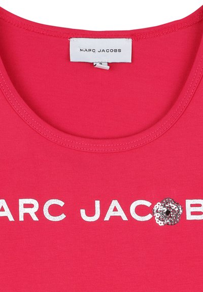 Chemise en coton rose avec un col rond, arborant un texte blanc audacieux "MARC JACOBS" et un détail de fleur en sequins argentés sur la gauche.