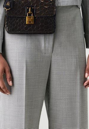 Pantalon taille haute à carreaux noirs et blancs avec devant plat, associé à un sac à main en cuir noir embossé avec une fermeture dorée.