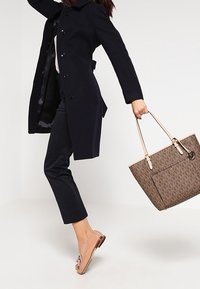 Manteau en laine marine, pantalon noir à motifs, ballerines marron clair et sac fourre-tout tan avec des bretelles, doté d'une poche avant.