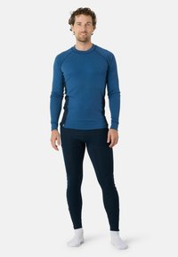 Chemise thermique à manches longues bleue avec une texture côtelée et des panneaux latéraux noirs contrastants, associée à des leggings thermiques bleu foncé. Les chaussettes sont blanches.