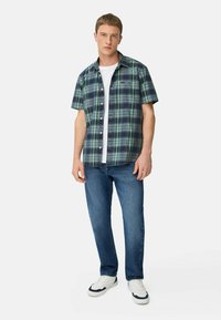 Korte mouwen geruite shirt in groen en marineblauw, met een knoopsluiting aan de voorkant, gecombineerd met blauwe jeans en witte sneakers.