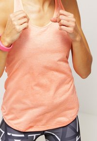 Peachfarvet top med rund kant og tynde stropper, fremstillet af let materiale. Tekstureret overflade, parret med mønstrede leggings.