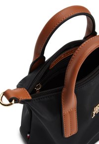 Μαύρη τσάντα χειρός από νάιλον με καφέ δερμάτινες λαβές, χρυσά κατασκευαστικά στοιχεία και κλείσιμο με φερμουάρ. Διαθέτει λεία υφή και δομημένο σχήμα.