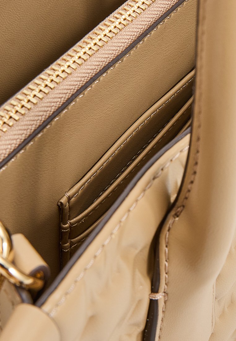 Intérieur d'un sac à main beige montrant un compartiment zippé et des emplacements pour cartes ; texture en cuir lisse et détails de fermeture éclair en ton doré.