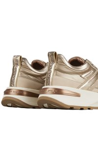Een paar metallic gouden en beige sneakers met witte zolen en bruine accenten, voorzien van het merk 'Alexander Smith' op de hiel en het trekbandje.