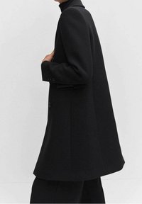 Sort uldblandingsfrakke med et struktureret design, lange ærmer og knapdetaljer. Har en let udvidet silhuet og høj krave.