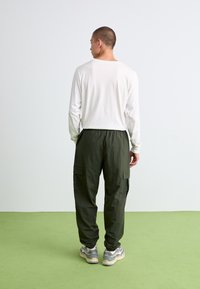 Langærmet hvid skjorte kombineret med mørkegrøn cargo-bukser, der har sidelommer. Modellen bærer grå sneakers. Simpelt, funktionelt design.