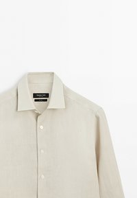 Beige long-sleeve linen shirt with a pointed collar and front buttons, hanging against a white background.