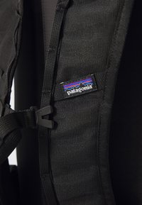Crna torba na leđa izrađena od izdržljive tkanine, s podesivim trakama i oznakom logotipa Patagonia. Dizajn naglašava funkcionalnu opremu i šavove.
