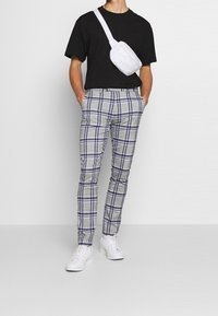 Harmaat ruutuhousut, joissa on tummansinisiä viivoja, kapea malli. Yhdistetty mustan t-paidan ja valkoisen olkapussin kanssa. Valkoiset lenkkarit viimeistelevät asun.