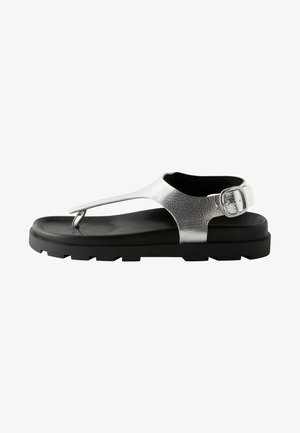 Metallic silver synthetic sandals with a textured strap, black rubber sole, and adjustable buckle. Minimalist design with a T-strap.