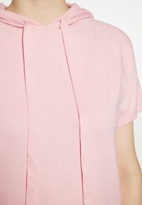 Lichtroze hoodie met korte mouwen, voorzien van een trekkoord en ribgebreide details, gemaakt van een zachte, gestructureerde stof. Het heeft een relaxte pasvorm en raglanmouwen.