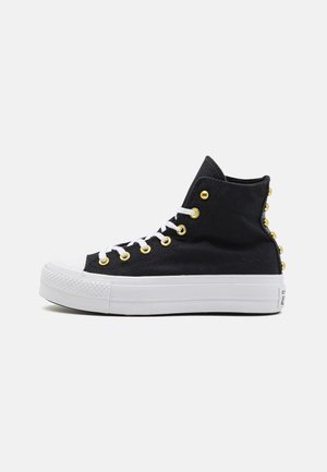 Schwarze High-Top-Sneaker mit weißer Sohle, goldenen Ösen und dekorativen Nieten auf der Rückseite. Hergestellt aus einem Struktur-Canvas-Material.