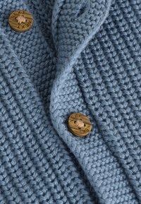 Cardigan tricoté bleu clair avec un motif de points texturé, doté d'un bouton rond marron clair gravé de "NEXT" et d'un col plié.