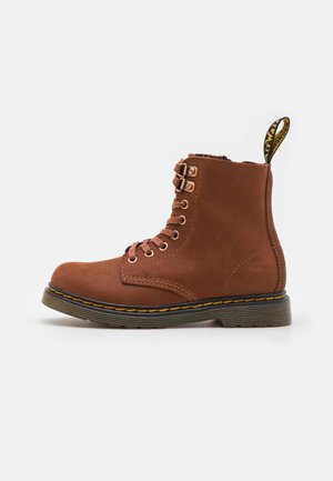 Bota corta de cuero marrón con cordones, costuras amarillas, suela negra y lengüeta con logo en el talón sobre un fondo blanco.