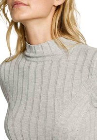 Svetarja svetlo siva, rebrasta turtleneck iz mehkega pletenega materiala, ki ima visok ovratnik in diagonalni vzorec.