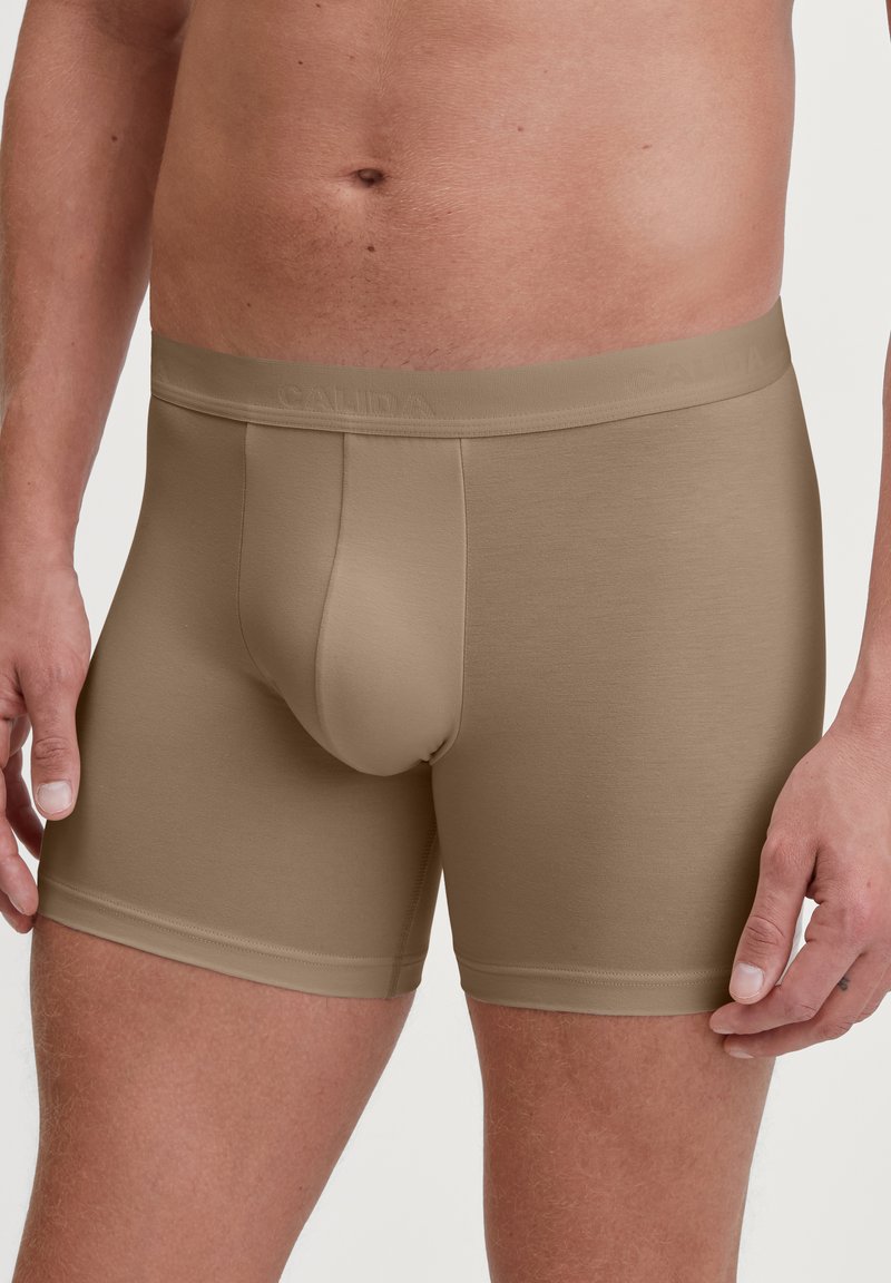 Boxer briefs da uomo in un colore marrone chiaro. Realizzati in tessuto morbido, presentano un elastico soffice con marchio in rilievo e una tasca sagomata.