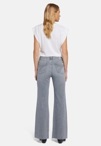Jean flare taille haute en denim gris clair avec un ourlet effiloché. Associé à un haut blanc court, offrant une coupe décontractée et des détails minimalistes.