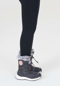 Sorte vinterstøvler med grå pelskant, gummisåler og snørebånd. Prydet med et rundt emblem. Bæres med sorte leggings.