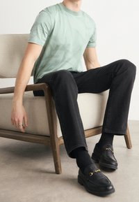 Mintunvihreä T-paita, jossa on hienovarainen aaltoilu, yhdistettynä mustiin suoriin housuihin ja mustiin nahkalouvisiin, joissa on kultaiset yksityiskohdat.