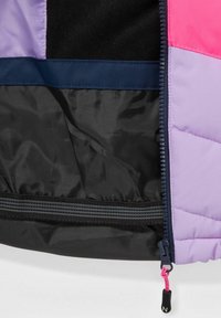 Veste isolante présentant des panneaux violets, roses et noirs, un extérieur lisse et brillant, un tissu texturé, et une poche zippée avec une languette de tirage.