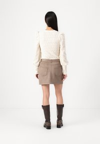 Vit, texturerad topp med puffärmar och geometriskt mönster, i kombination med en beige mocka mini-kjol med två bakfickor. Bruna knähöga stövlar.