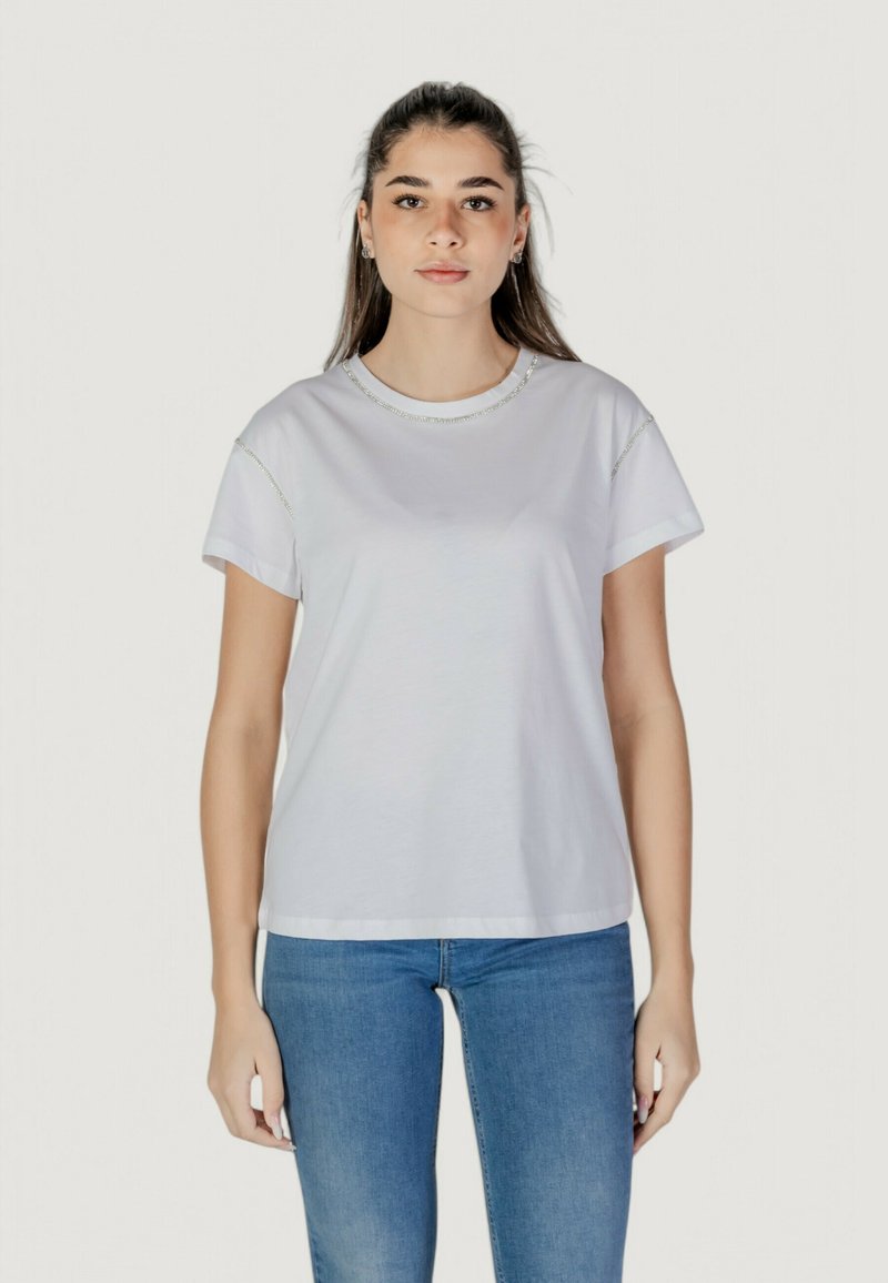 Camiseta blanca de manga corta con un cuello redondo y un sutil bordado decorativo a lo largo del cuello y los hombros. Tejido de algodón texturizado.