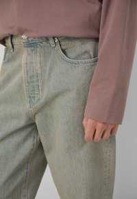 Lys blå denim jeans med en falmet finish, med en frontlomme, og en ensfarvet, afdæmpet lavendelfarvet langærmet skjorte båret ovenpå.