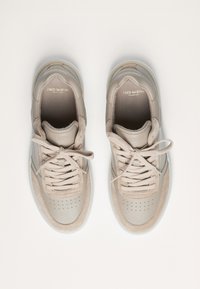 Zapatillas de cuero beige con una superficie suave, puntera perforada y cordones a juego. Presentan un logo sutil y una suela translúcida.