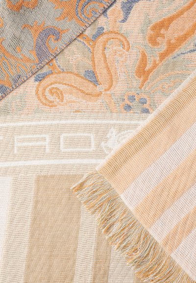 Textiles tissés beiges, orange et bleus partiellement pliés, avec des motifs floraux et géométriques, montrant la texture et des bords frangés.